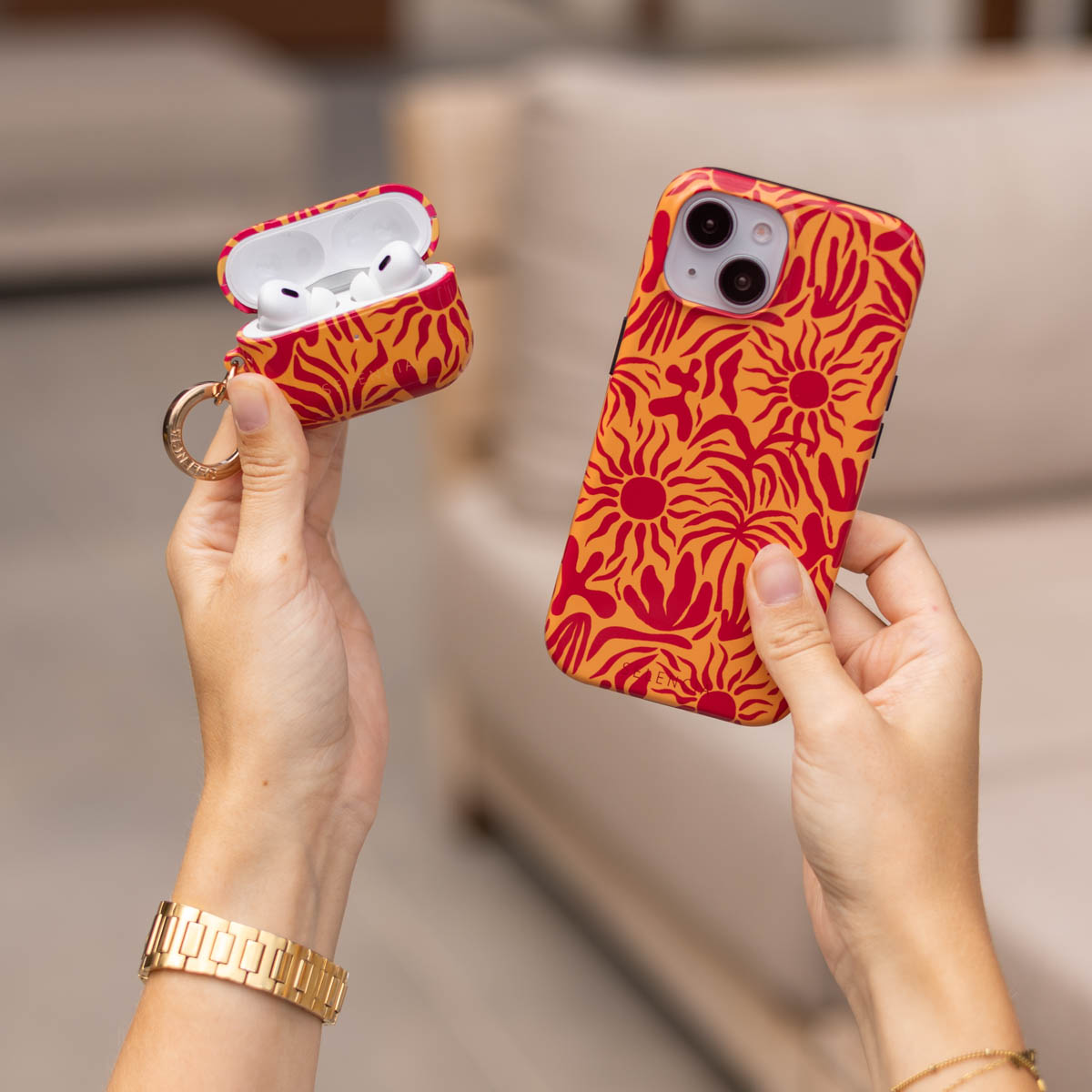 Mani tengono una custodia per telefono e una custodia per AirPods con motivo a raggiera rossa su sfondo arancione.