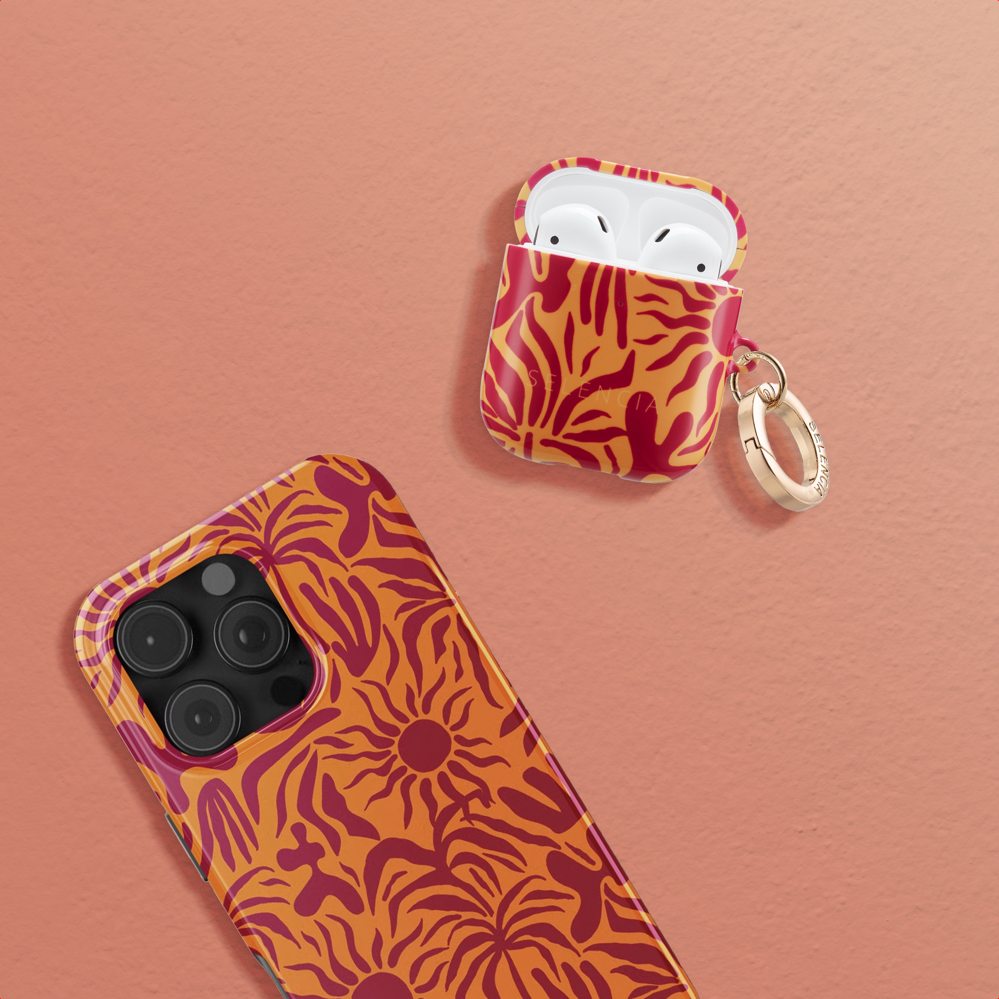 Una custodia per telefono arancione e una custodia AirPods con motivo rosso su sfondo corallo.