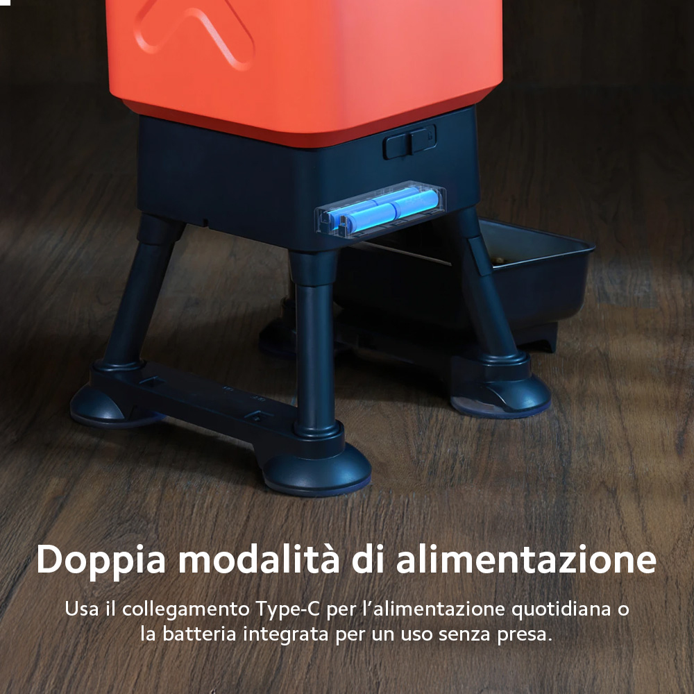 Un comedero automático para mascotas naranja y negro con baterías visibles, sobre suelo de madera.