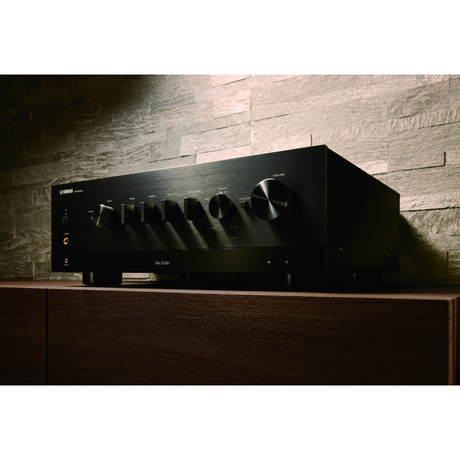 Schwarzer Yamaha Stereo-Verstärker mit silbernen Knöpfen auf einem Holzschrank.