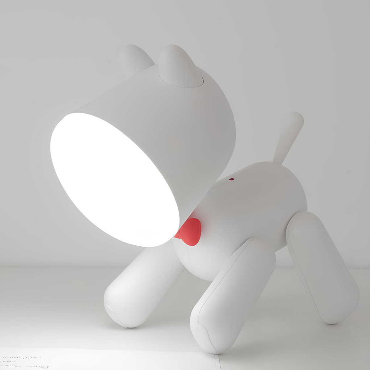 Eine weiße Schreibtischlampe in Hundeform mit roter Fliege steht auf weißer Fläche.