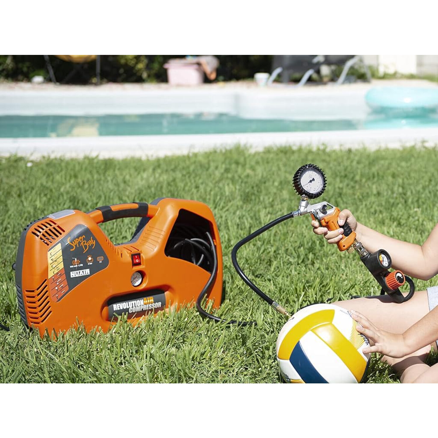 Compressore d'aria arancione sull'erba vicino alla piscina, gonfia pallone volley.