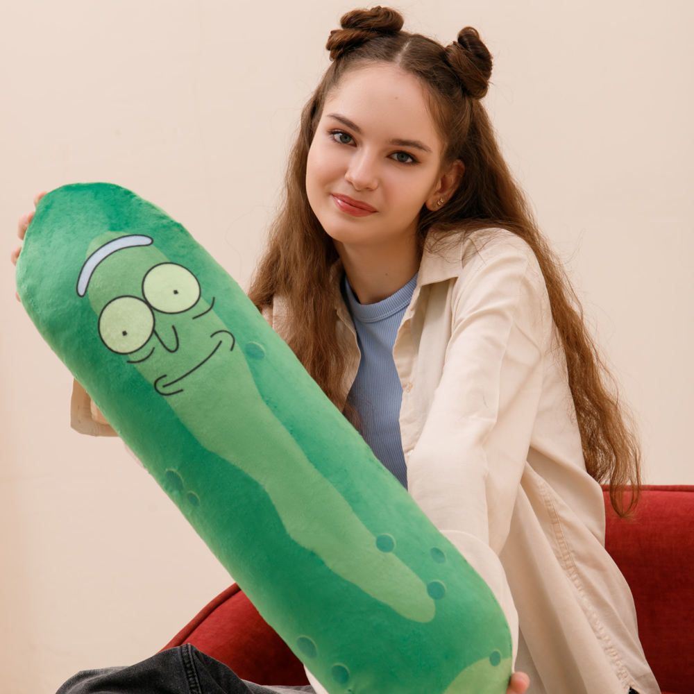 Ein Mädchen hält ein Rick-und-Morty-Kissen in Form einer Gurke. Sie sitzt auf einem roten Sofa.