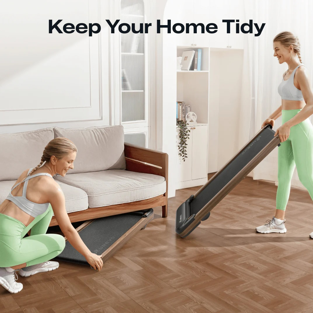 Dwie kobiety sprzątają salon, chowając bieżnię pod kanapą.