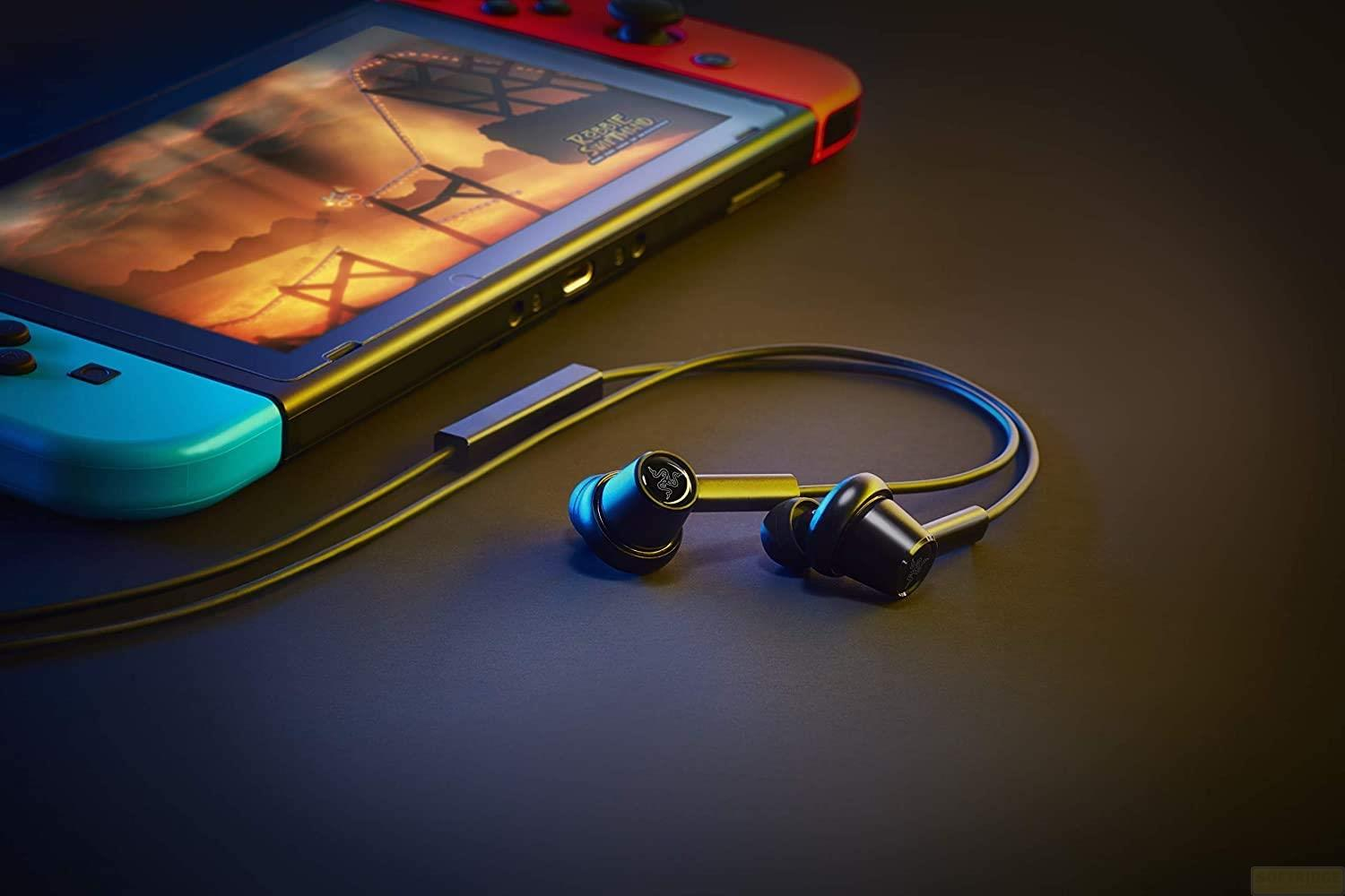 Une Nintendo Switch et des écouteurs reposent sur une surface sombre.