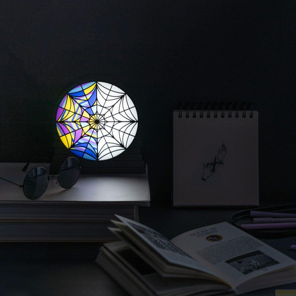 Una lámpara redonda de vidrieras con telaraña y secciones moradas, amarillas y azules está sobre libros.