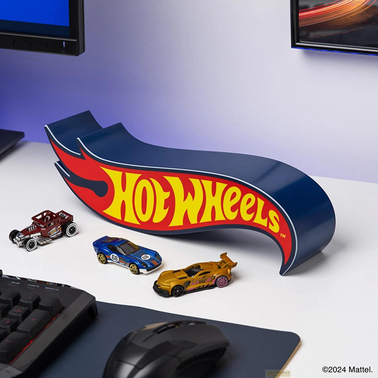 Wystawa z logo Hot Wheels i trzema samochodzikami na biurku, obok klawiatury i myszy.