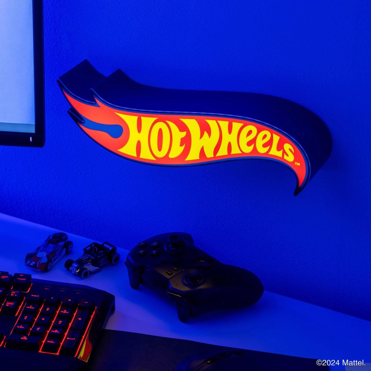 Logo Hot Wheels na niebieskiej ścianie nad klawiaturą, kontrolerem i autkami.