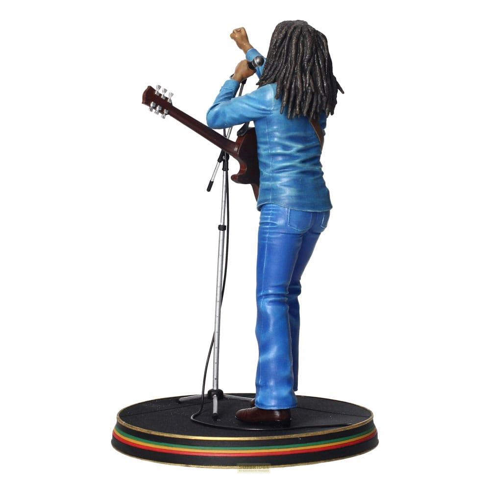 Figura de Bob Marley con rastas, camisa azul, jeans, sosteniendo guitarra y cantando.