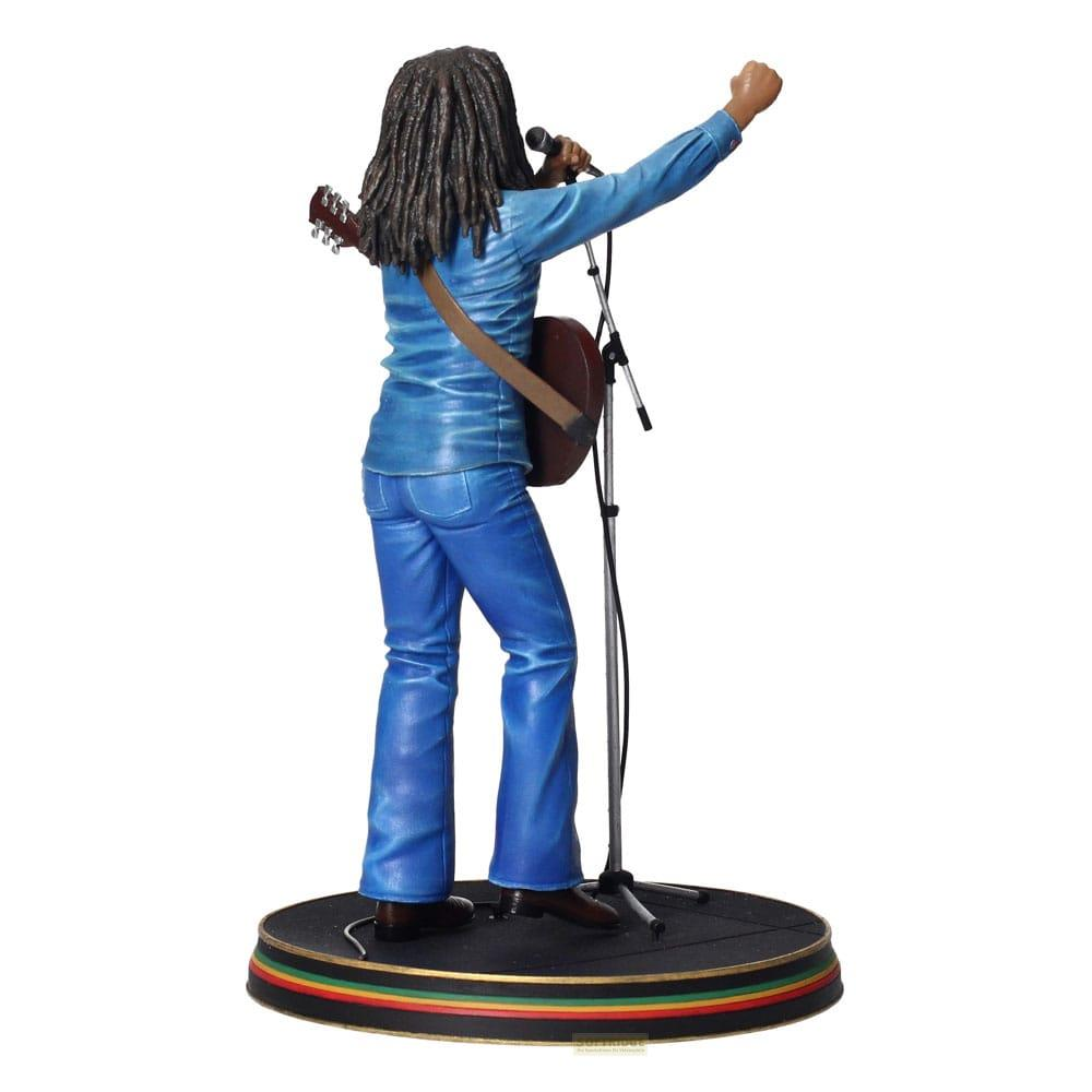 Figura de Bob Marley cantando con guitarra, con camisa y jeans azules, en escenario con micro.