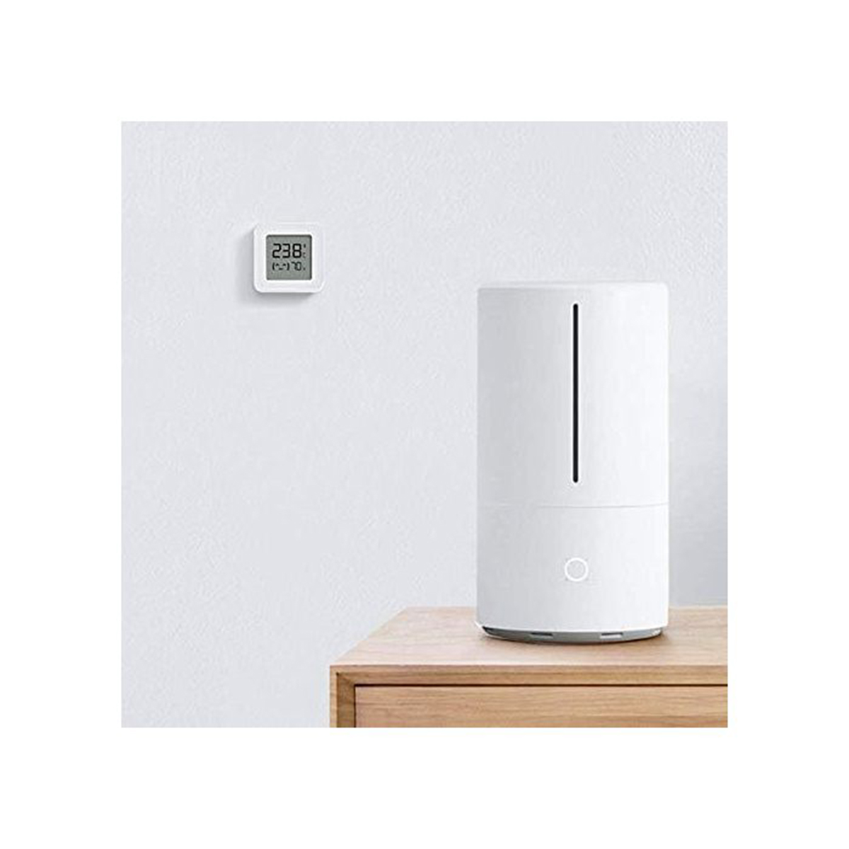 Un termómetro digital blanco cuelga de una pared blanca junto a un humidificador blanco alto.