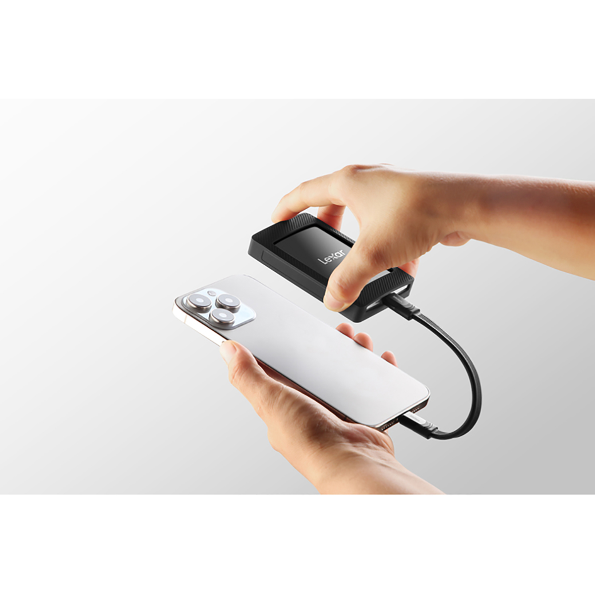 Dłonie podłączają przenośny dysk SSD Lexar do srebrnego iPhone'a kablem USB-C.