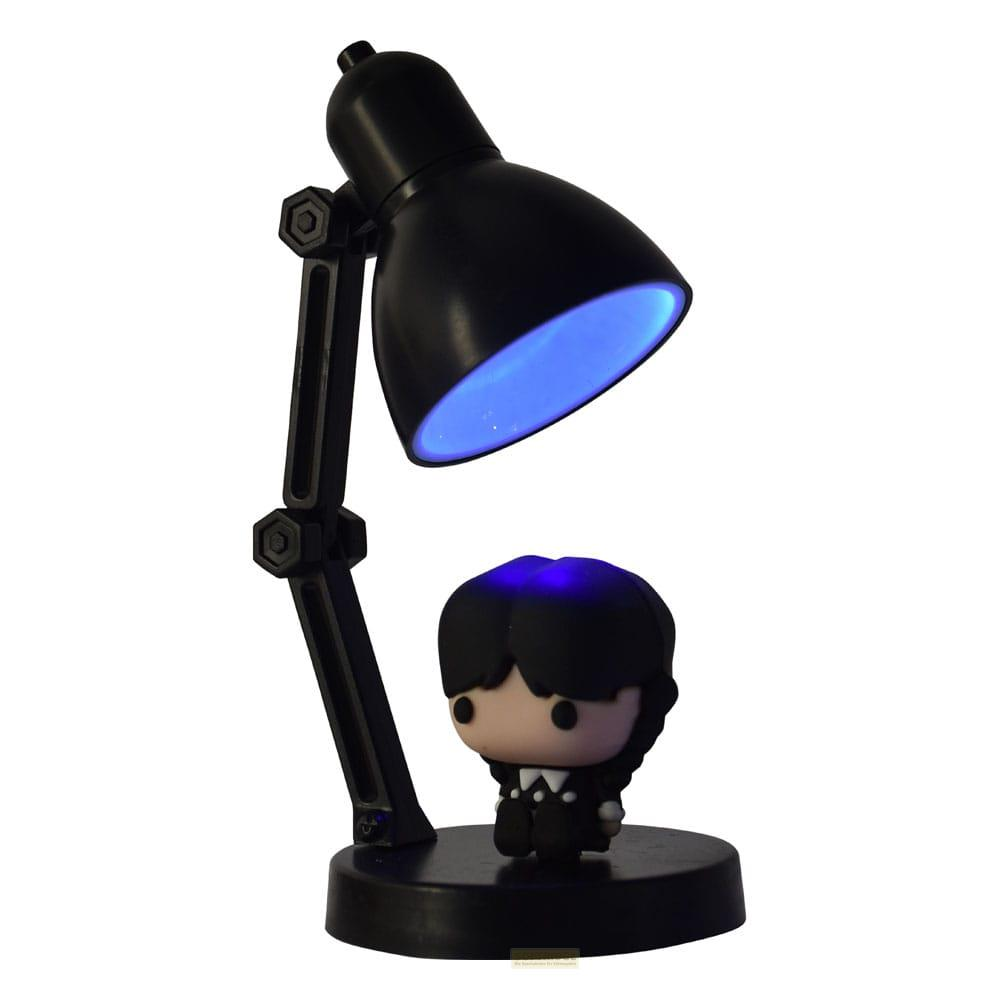 Una lámpara de escritorio negra con luz azul ilumina una pequeña figura de Wednesday Addams.