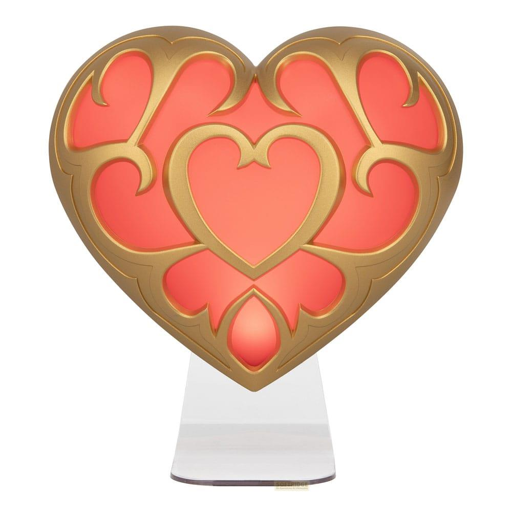 Una lámpara en forma de corazón con borde dorado y interior rosa brillante, sobre un soporte transparente.