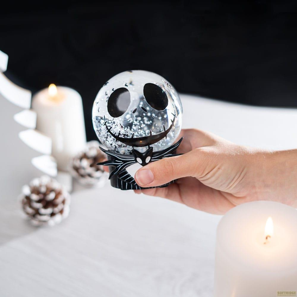 Eine Hand hält eine Jack Skellington-Schneekugel mit Glitzer. Kerzen und Tannenzapfen umgeben sie.