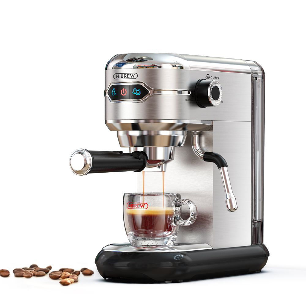 Una cafetera espresso plateada prepara café en una taza de espresso de cristal, con granos de café cerca.
