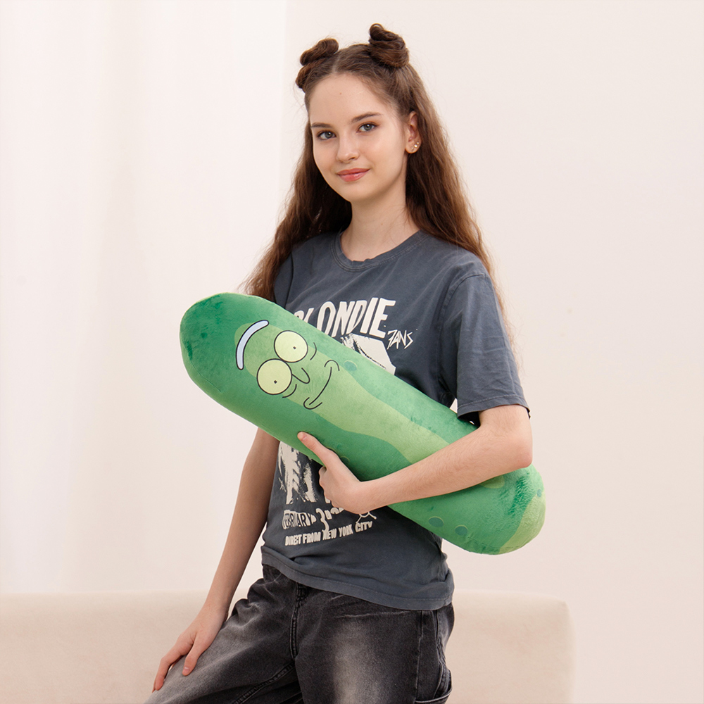 Ein Mädchen hält ein grünes Pickle-Plüschtier mit Gesicht. Sie trägt ein dunkles T-Shirt.