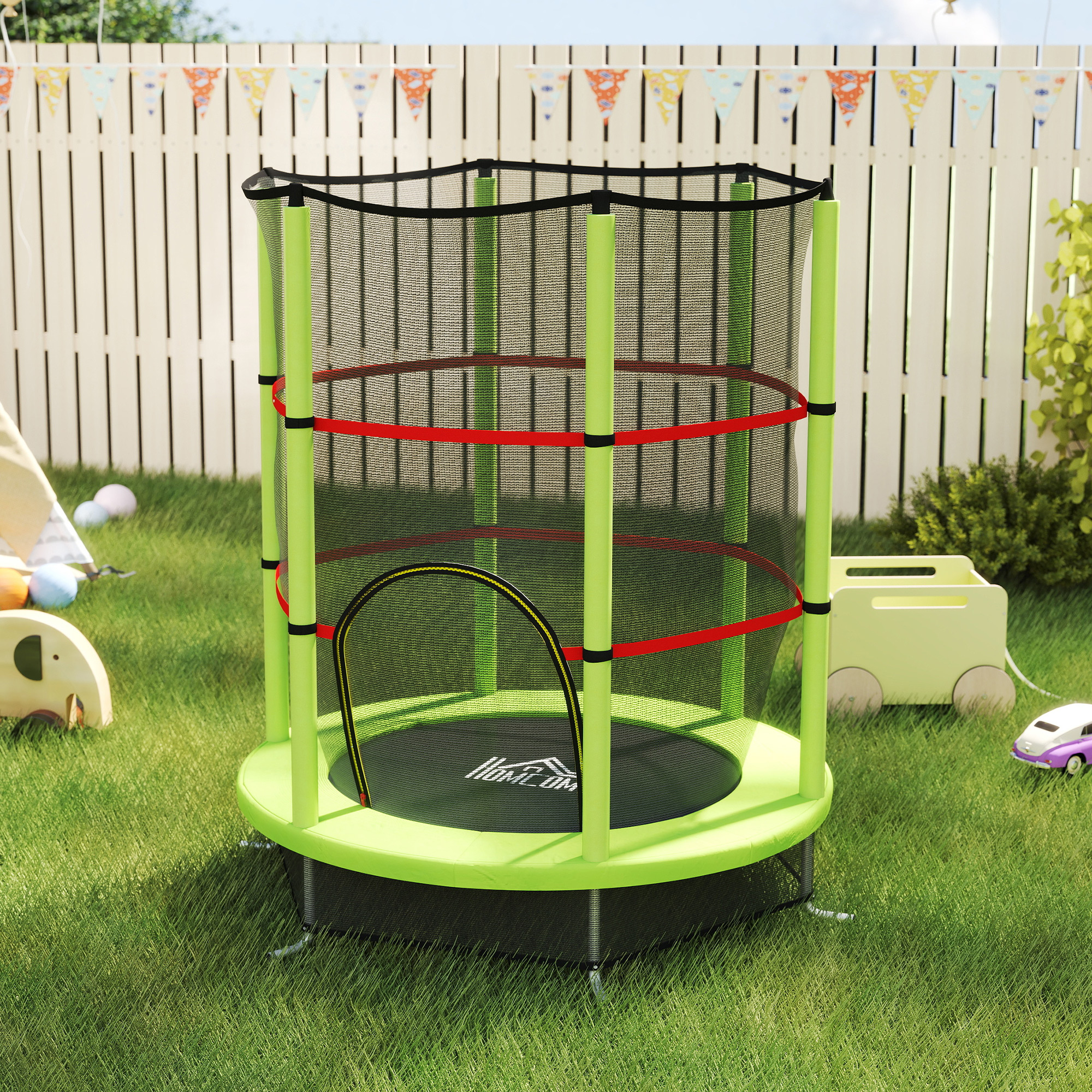 Un trampolino verde con rete di sicurezza si trova su un prato, con giocattoli e una recinzione.