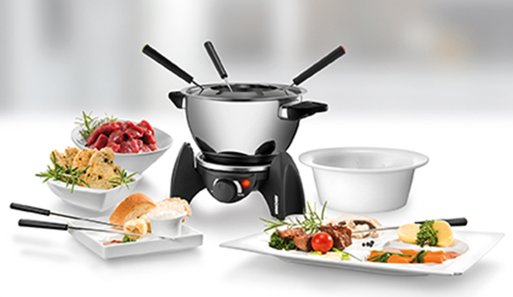 Zestaw do fondue z mięsem, chlebem, warzywami i serem na stole.