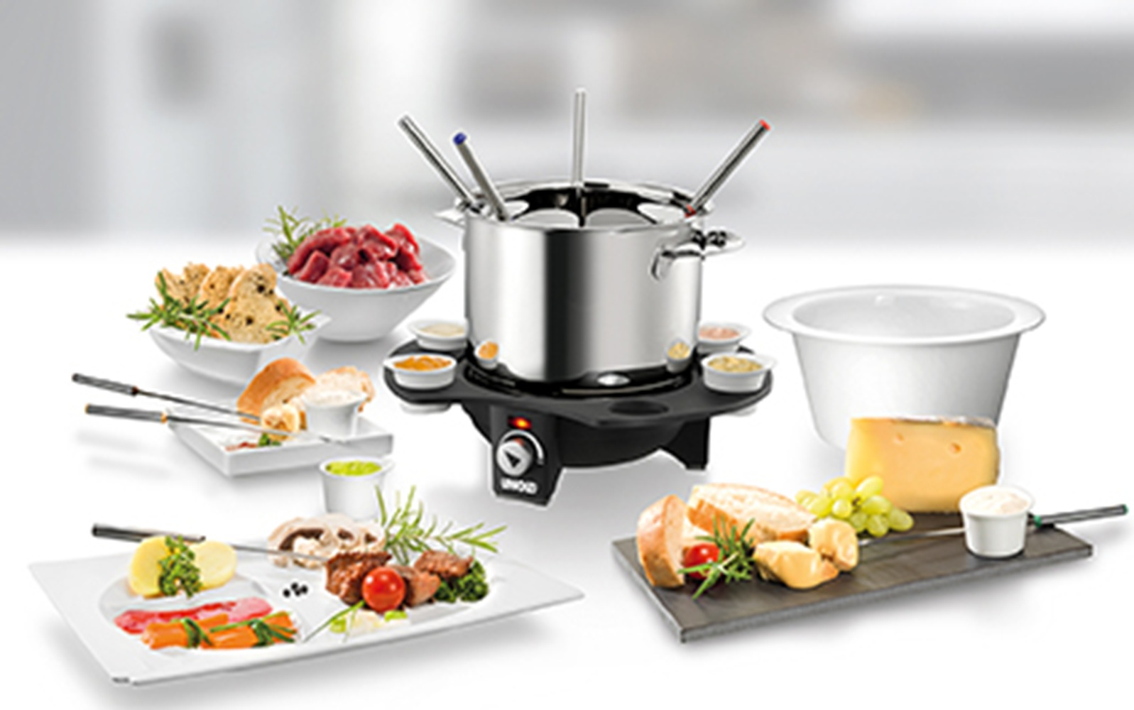 Ein Fondue-Set mit Fleisch, Brot, Käse, Trauben und Dips vor einem unscharfen Hintergrund.