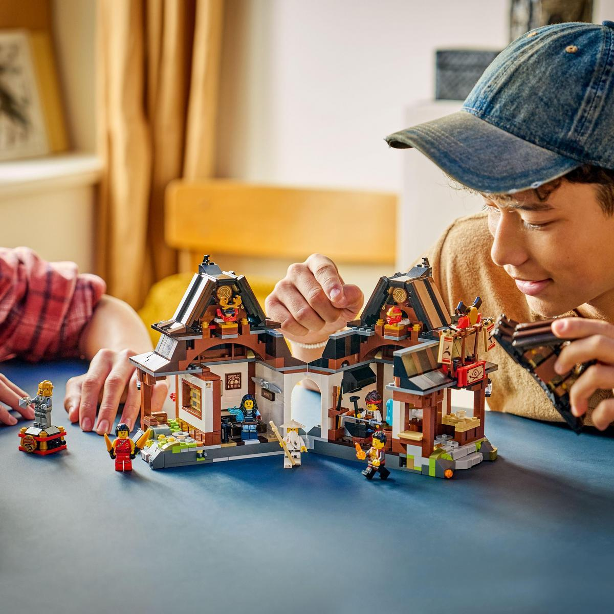 Çocuklar mavi bir masada Ninjago figürleriyle Lego ev yapıyor.