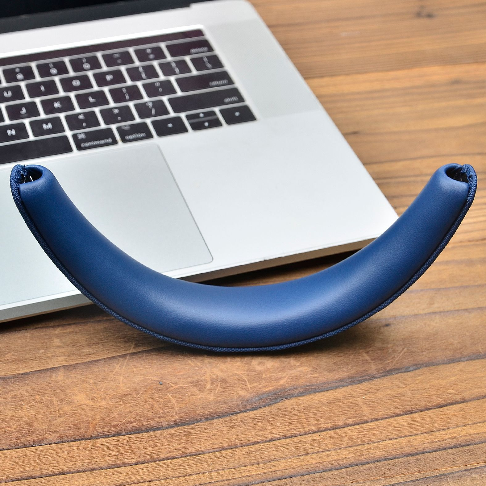 Niebieska poduszka słuchawek leży na otwartym srebrnym laptopie na drewnie.