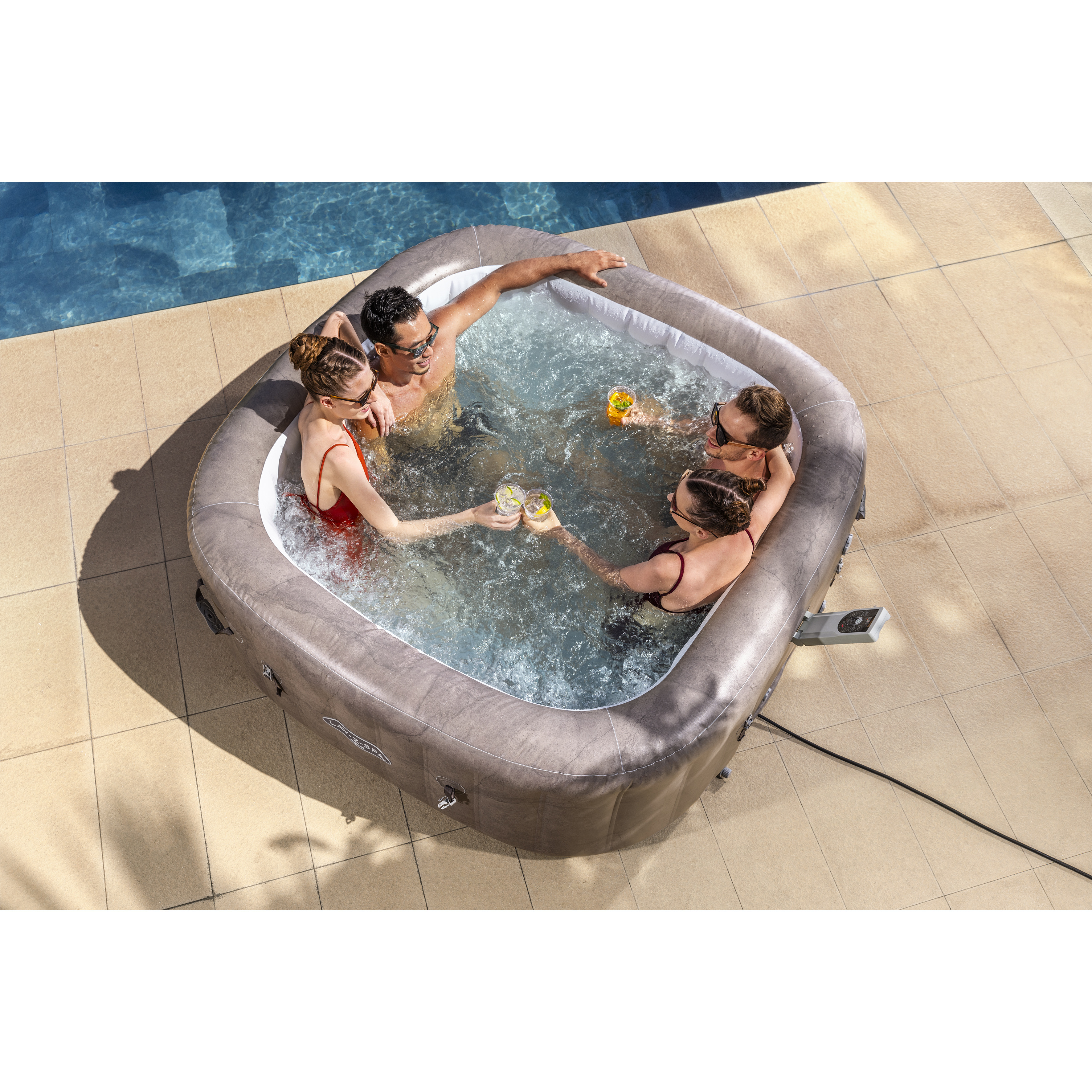 Vier Freunde in Badekleidung stoßen mit Getränken im Whirlpool auf einer gefliesten Terrasse an.