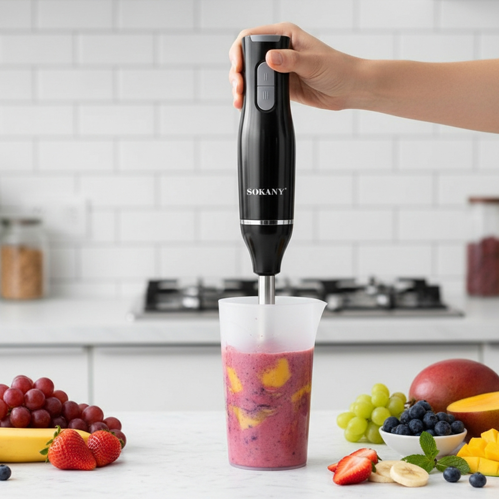 Schwarzer SOKANY-Handmixer mixt Obst in einem Becher. Obst umfasst Trauben, Erdbeeren, Banane, Mango, Blaubeeren.
