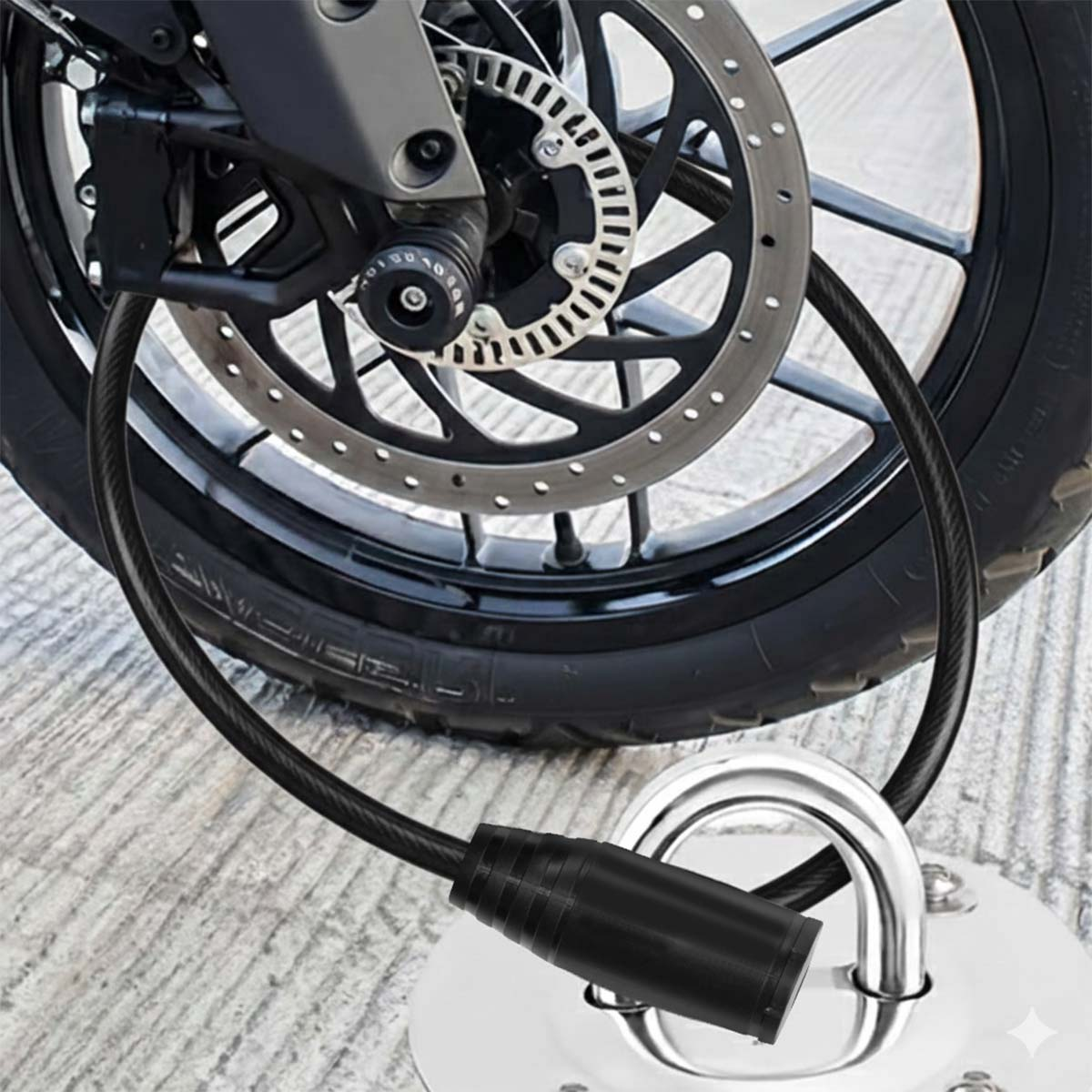 Ein schwarzes Kabelschloss sichert ein Motorradrad an einem Metallanker auf Beton.