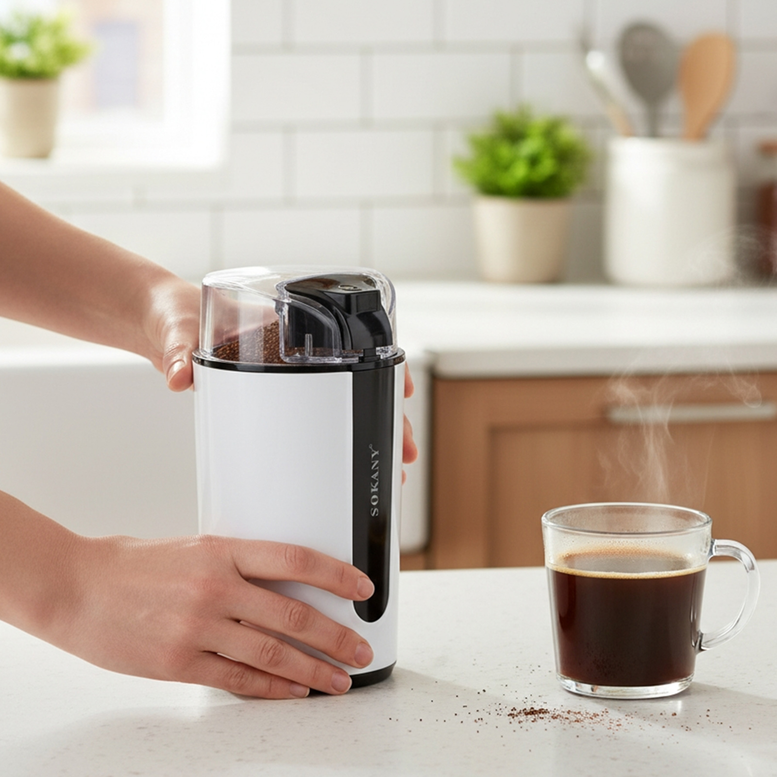 Hände halten weiße Kaffeemühle. Dampfende Kaffeetasse steht daneben.