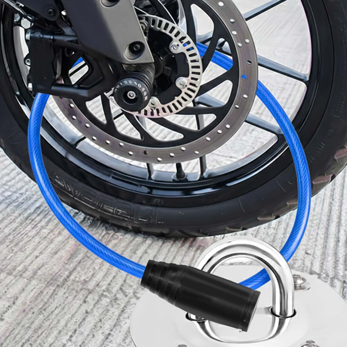 Blaues Kabelschloss an Motorradbremsscheibe und Metallbasis auf Beton befestigt.