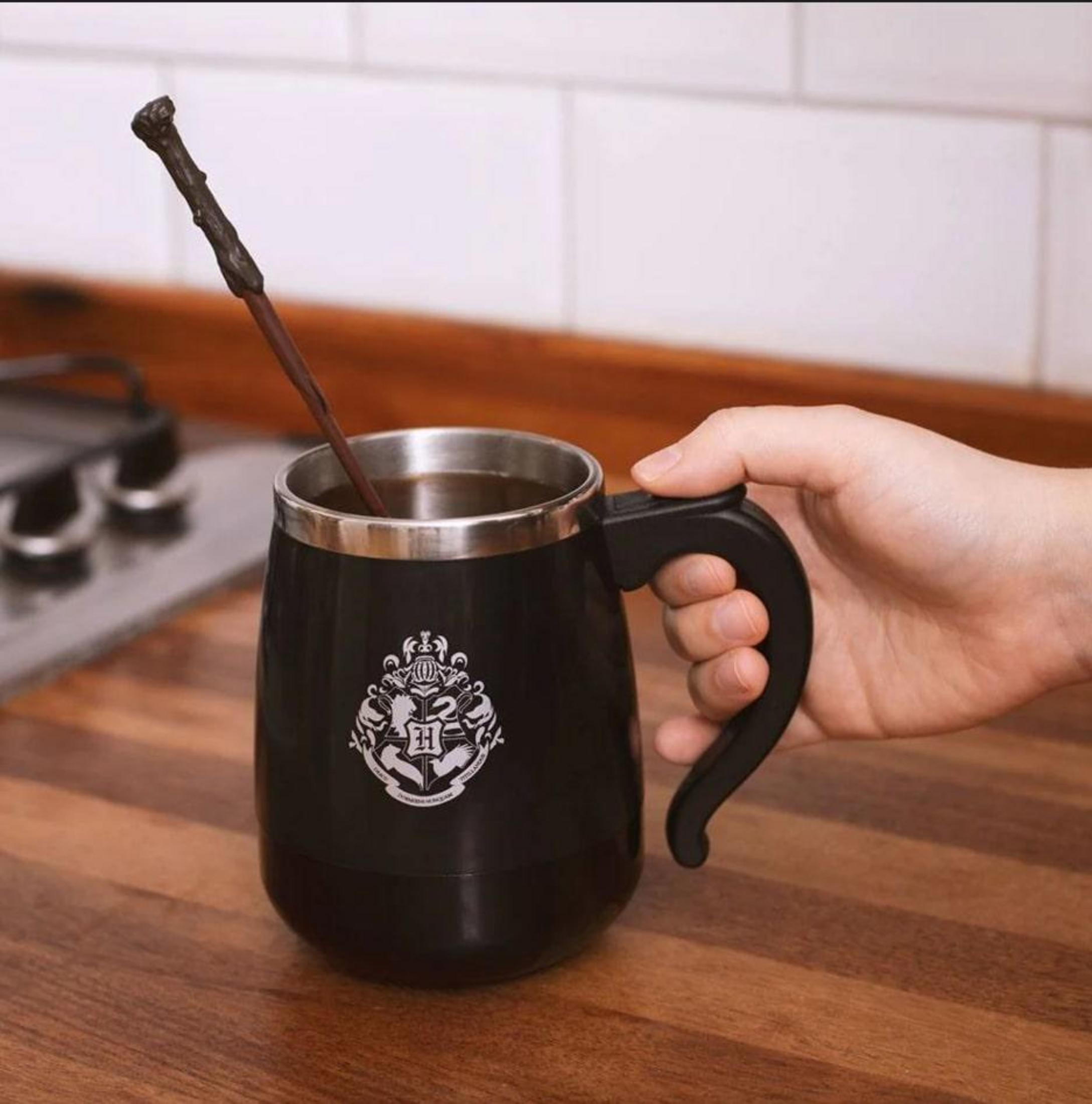 Une main tient une tasse noire avec une baguette à l'intérieur, sur une table en bois.