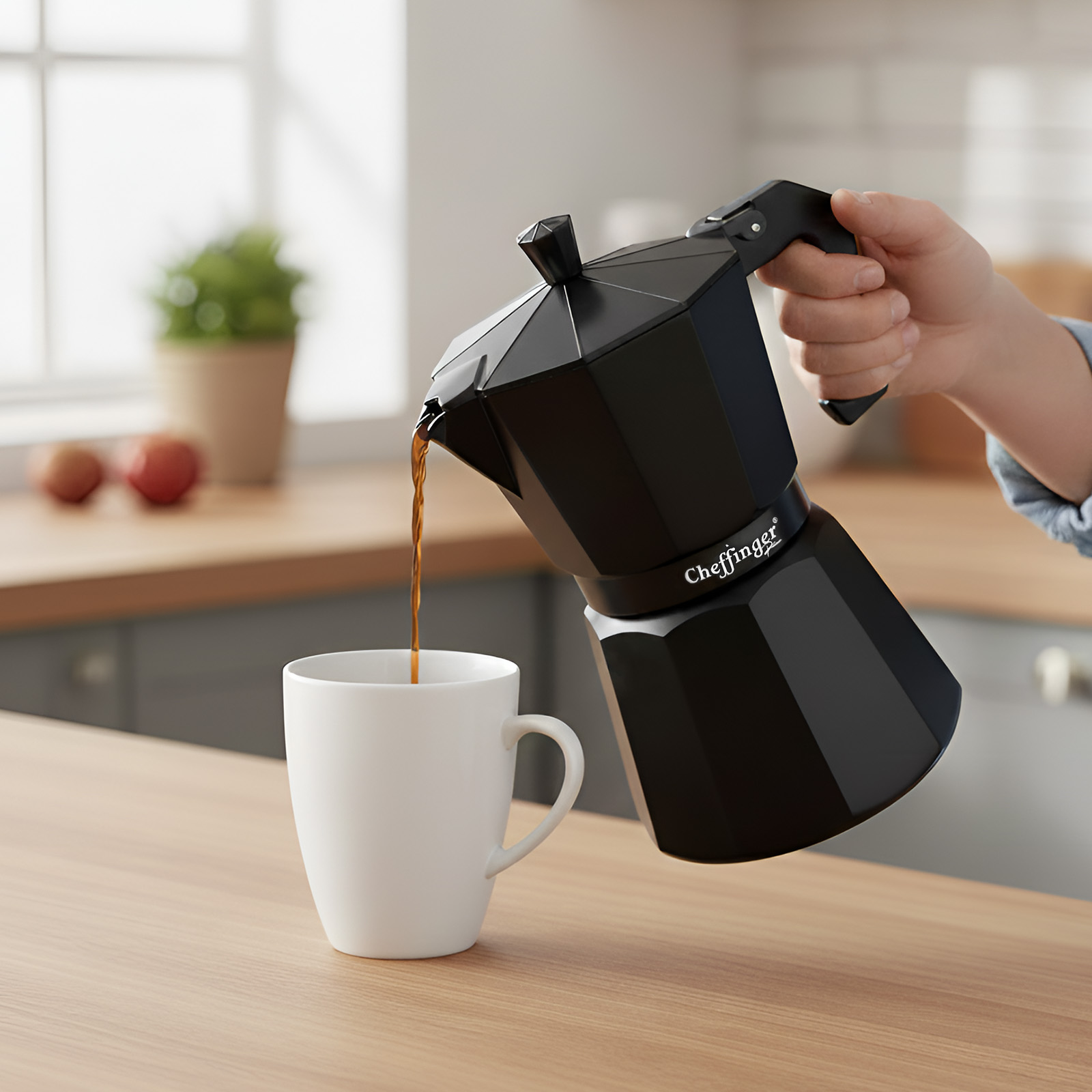 Una cafetera negra vierte café en una taza blanca sobre una mesa de madera.