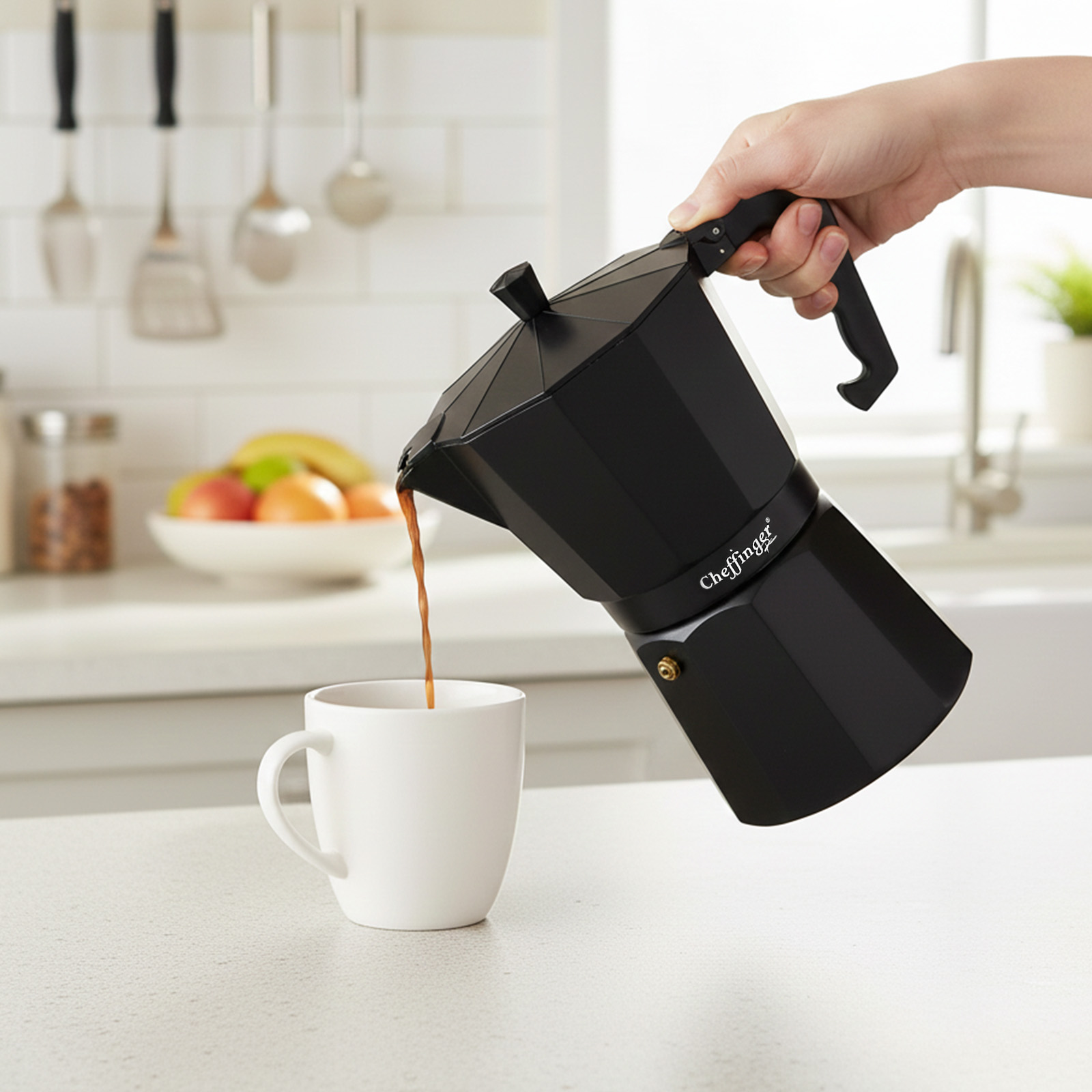 Una cafetera negra vierte café en una taza blanca en una cocina.