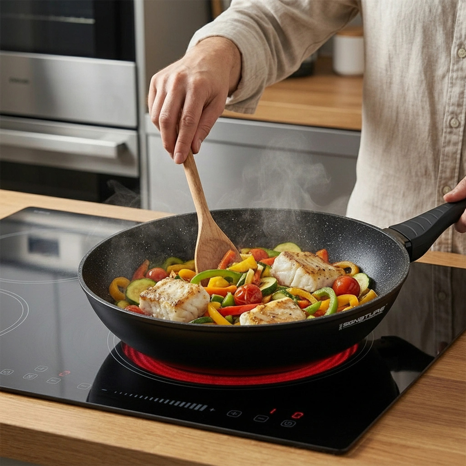 Une personne remue du poisson et des légumes colorés dans une poêle sur une plaque à induction.