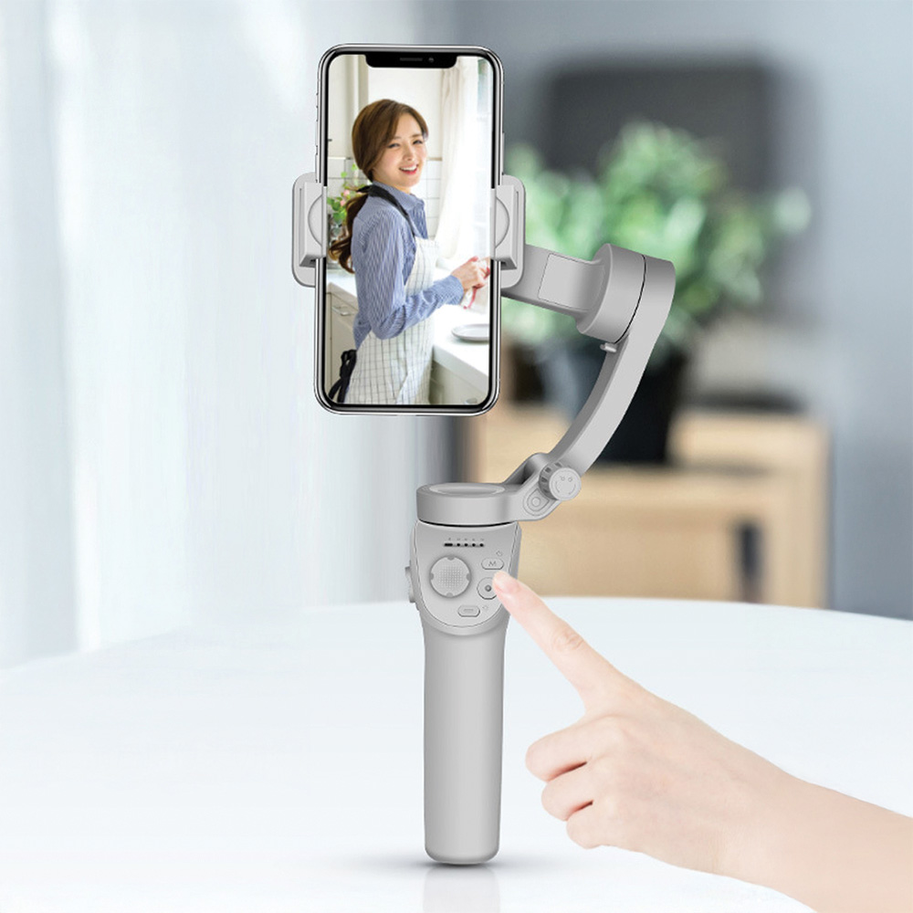 Bir el, ekranda bir kadın bulunan akıllı telefonu tutan gri bir gimbal üzerindeki düğmeye basıyor.