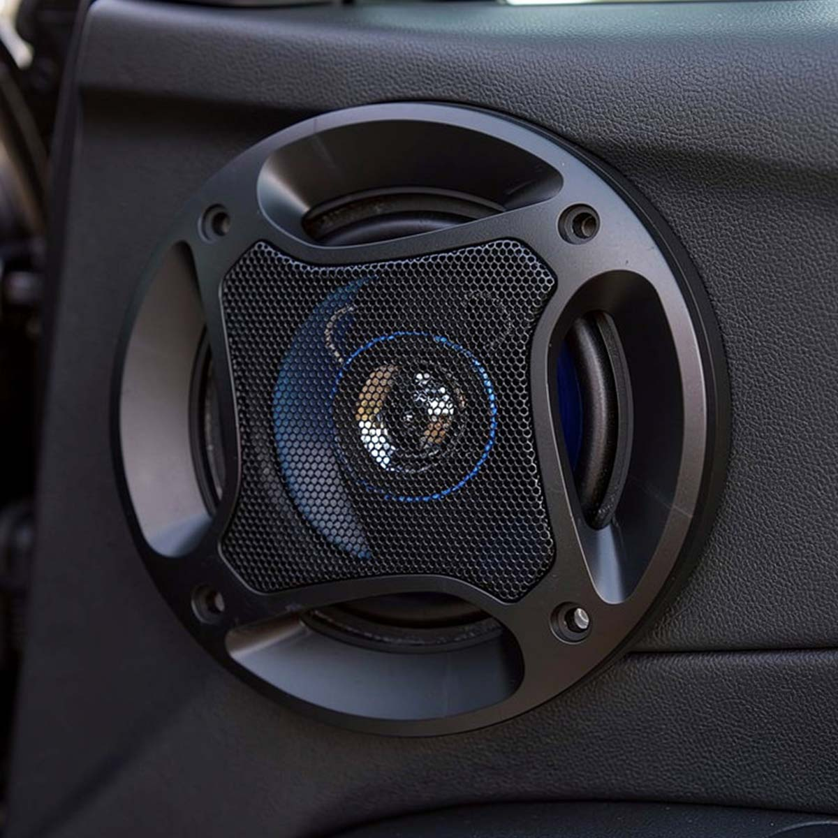 Gros plan d'un haut-parleur de portière de voiture noir avec grille en maille et accents bleus.