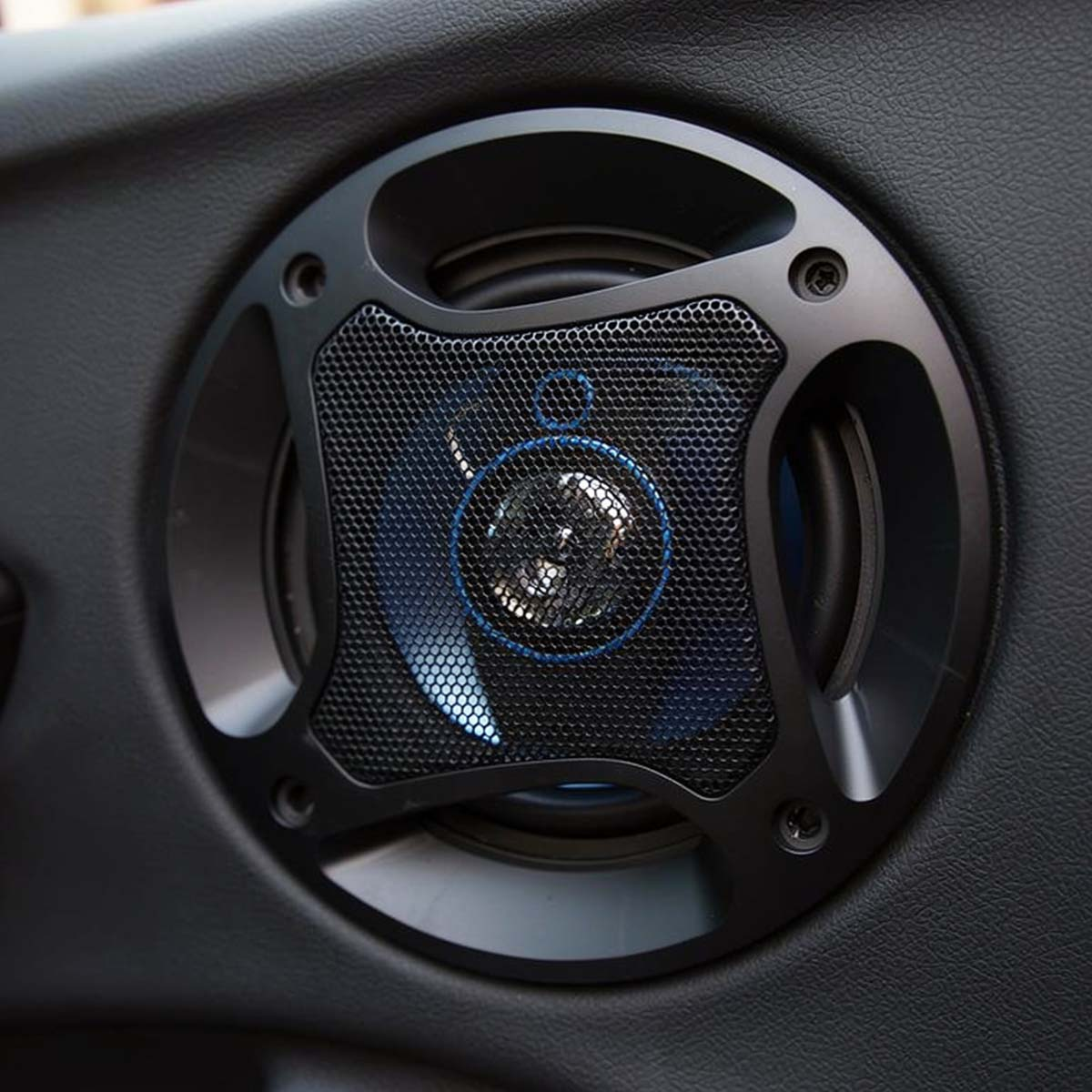 Un haut-parleur de porte de voiture noir avec une grille en maille et des accents bleus est visible.