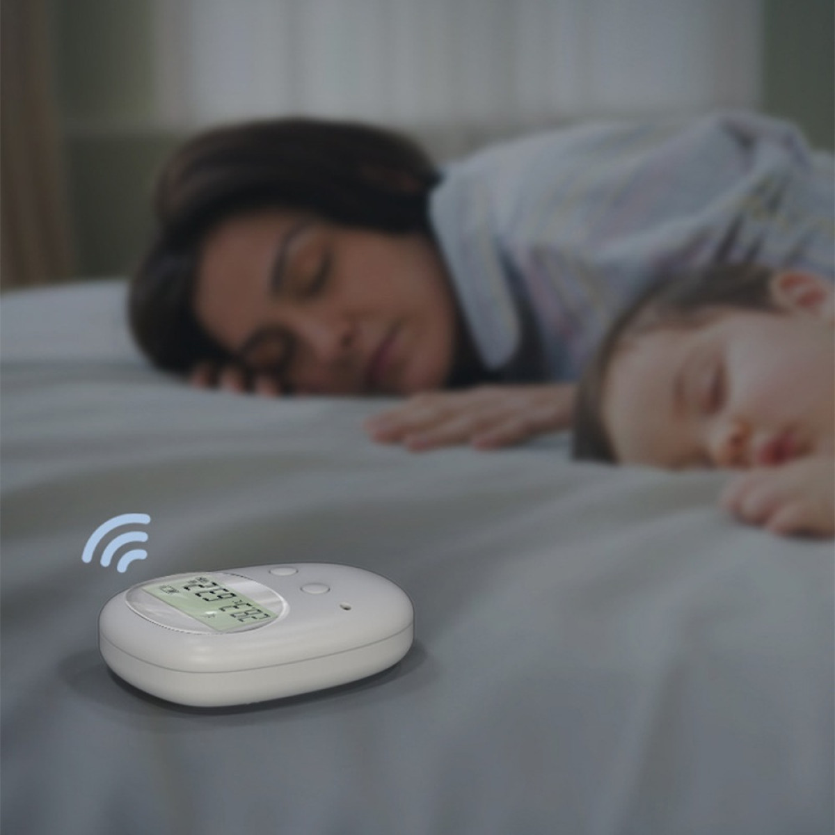 Ein Babyphone liegt auf einem Bett neben einer schlafenden Mutter und einem Baby.