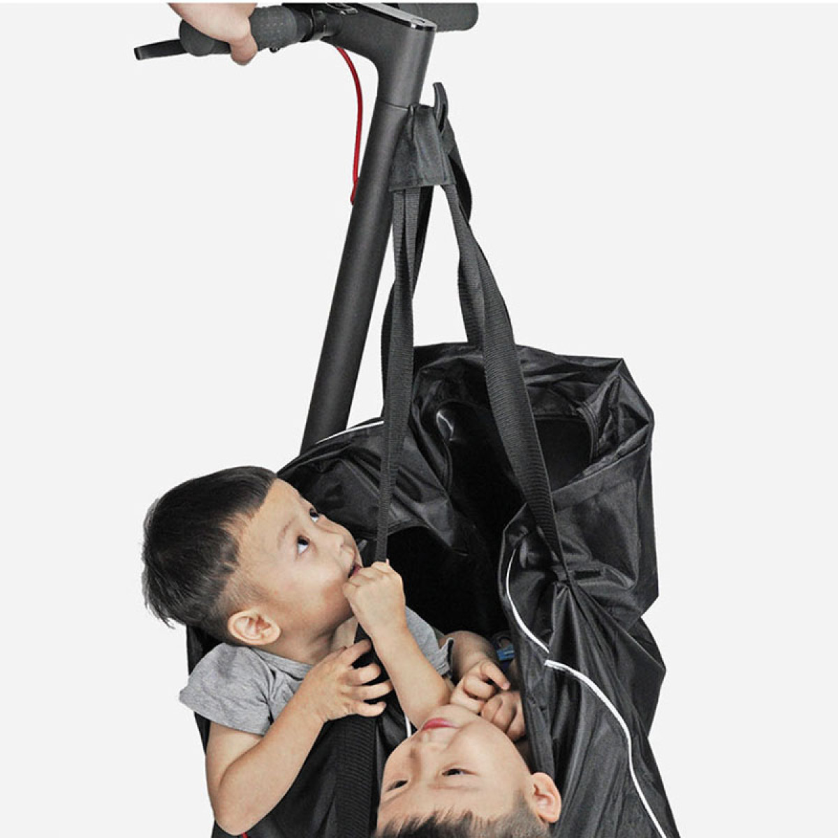 Dwóch małych chłopców w czarnej torbie wiszącej na kierownicy hulajnogi.