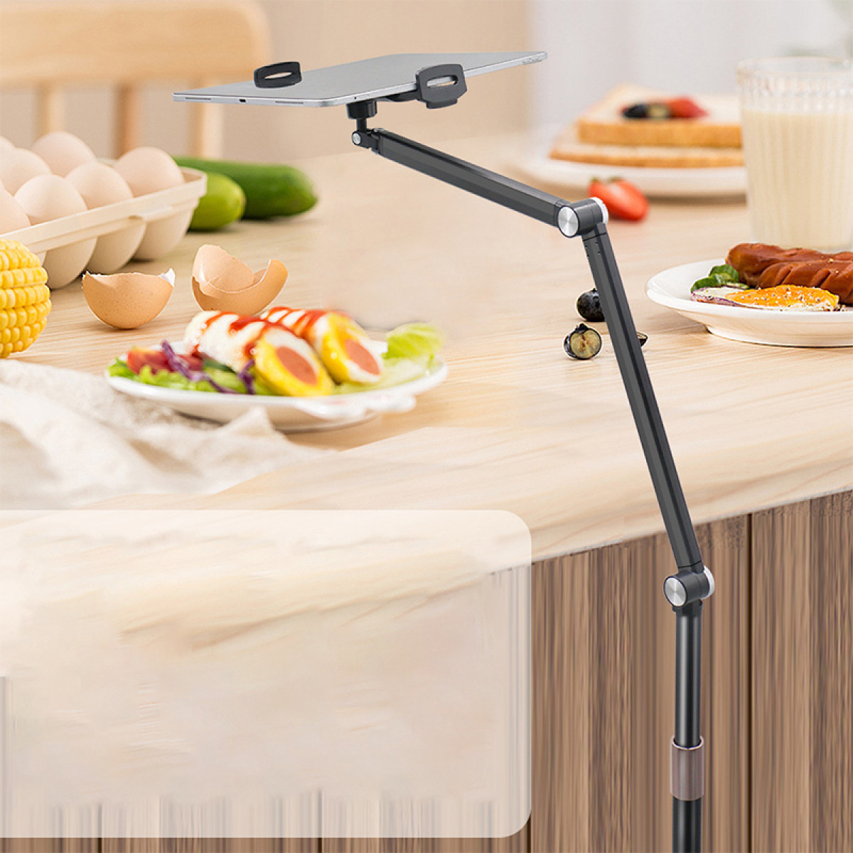 Stojak na tablet trzyma tablet nad stołem z produktami śniadaniowymi, takimi jak jajka, kiełbaski i tosty.