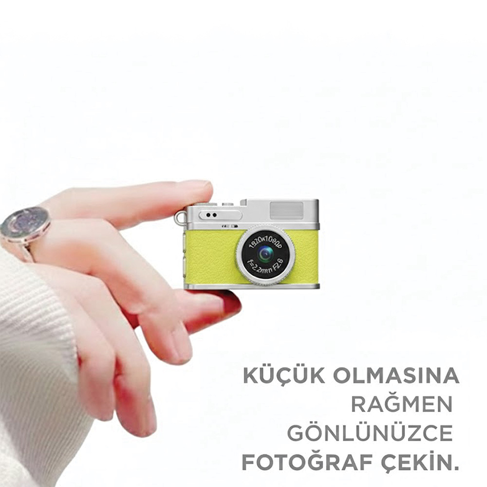 Bir el, gümüş aksesuarlı küçük, neon sarı dijital bir fotoğraf makinesi tutuyor.
