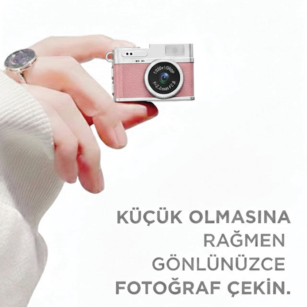 Bir kişi gümüş aksesuarlı küçük pembe bir kamera tutuyor.