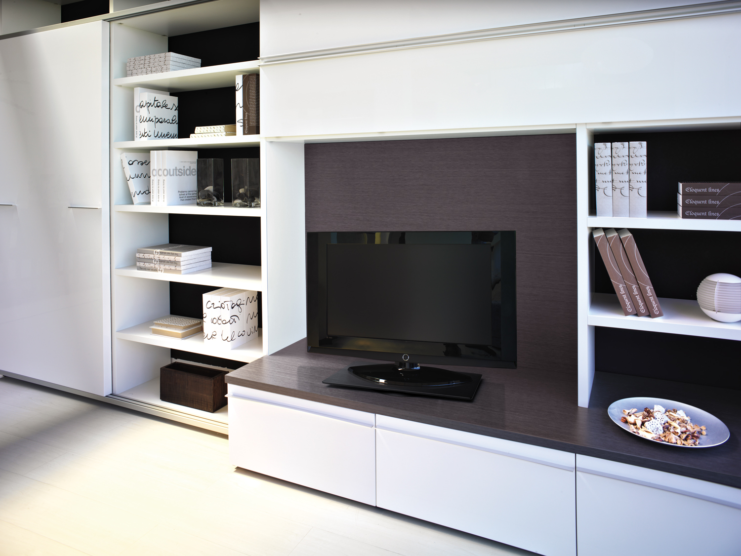 Moderna estantería blanca con TV, libros y objetos decorativos.
