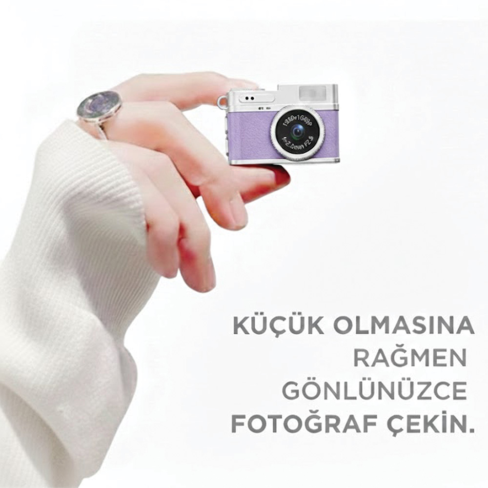 Bir el, beyaz gövdeli küçük, mor dijital fotoğraf makinesi tutuyor.
