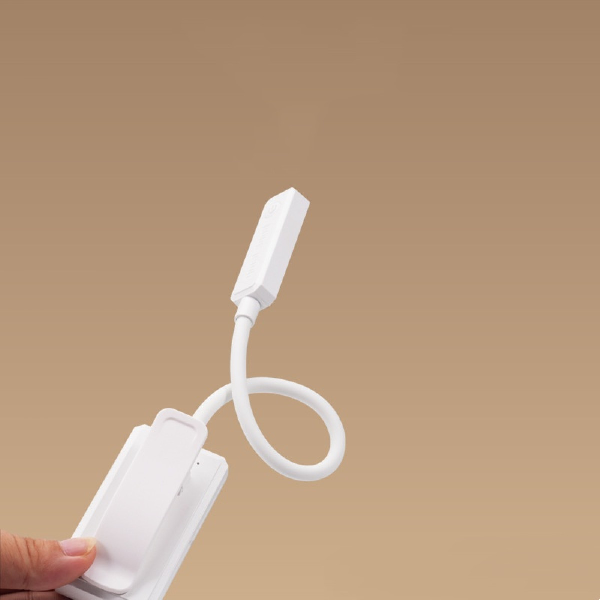 Biała lampka do czytania z klipsem i elastyczną szyjką jest trzymana przez dłoń.