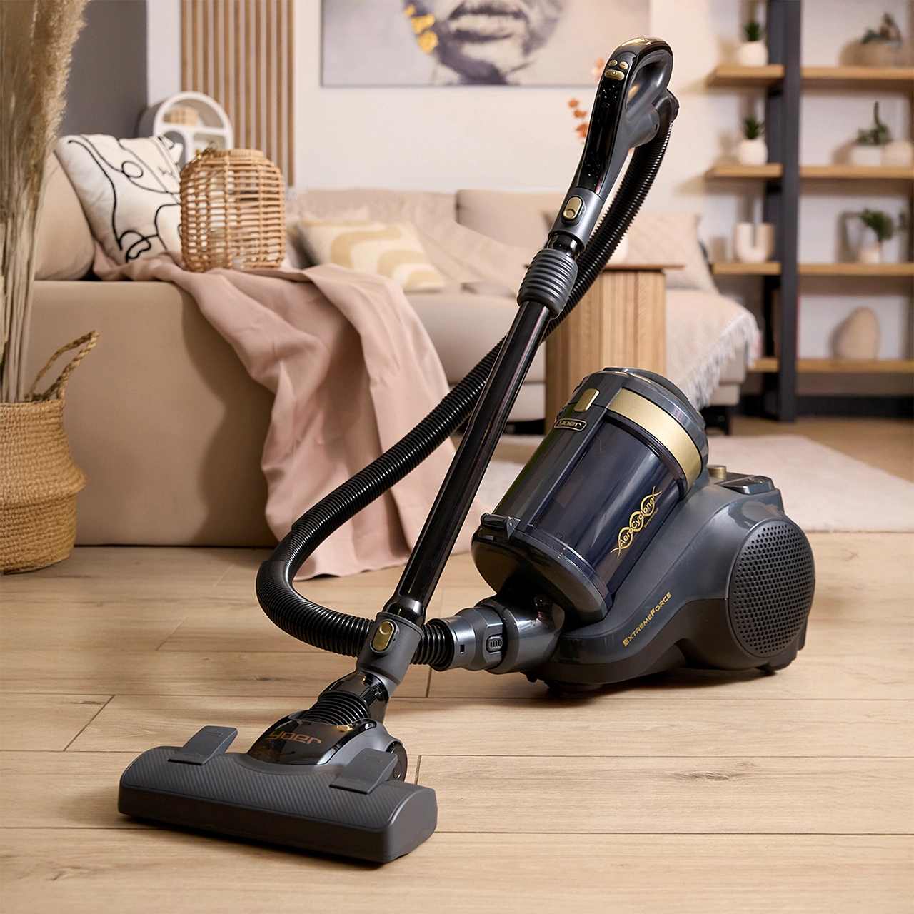 Nowoczesny szary odkurzacz na drewnianej podłodze z sofą w tle.