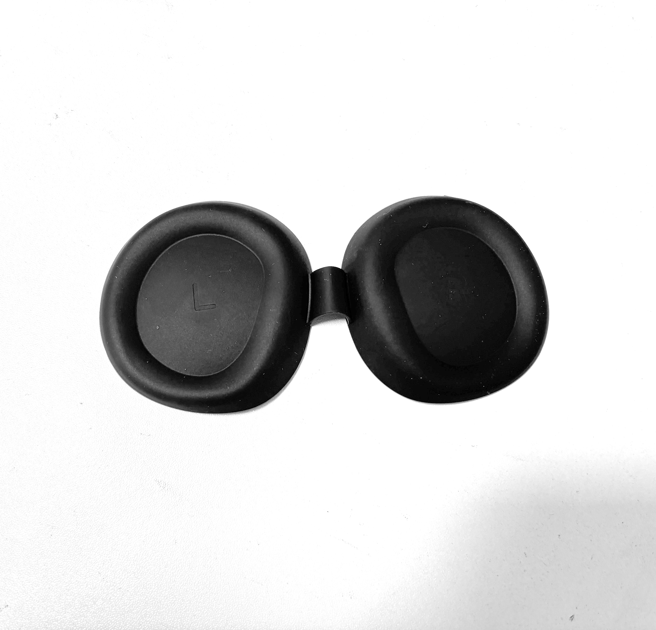 Dwie czarne gumowe końcówki słuchawek połączone małym zawiasem. Jedna końcówka ma "L".