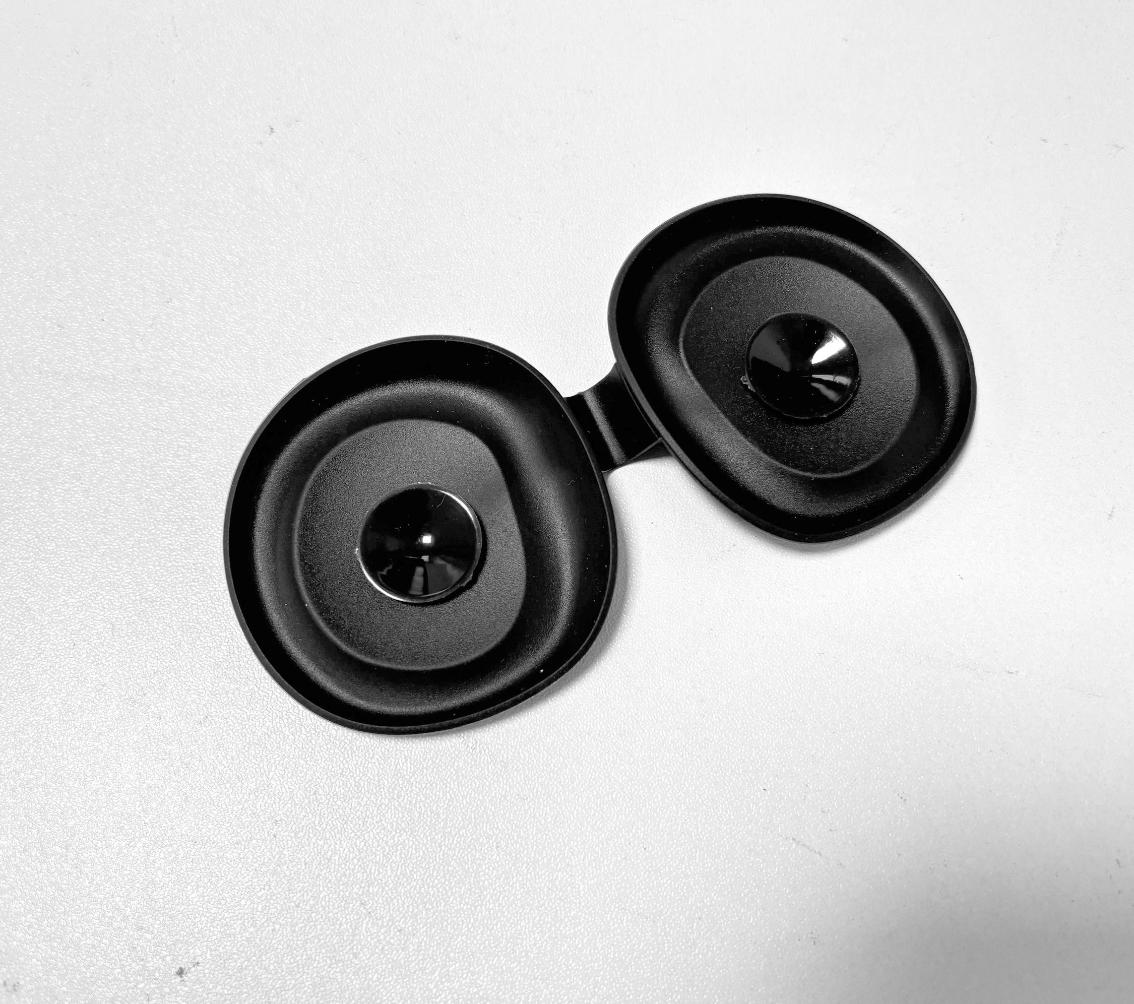 Dwa czarne, okrągłe słuchawki z błyszczącymi środkami leżą na białej powierzchni.