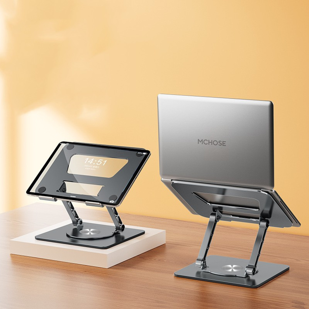 Dwa srebrne stojaki na laptopa na drewnianym stole. Jeden trzyma tablet, drugi laptop.